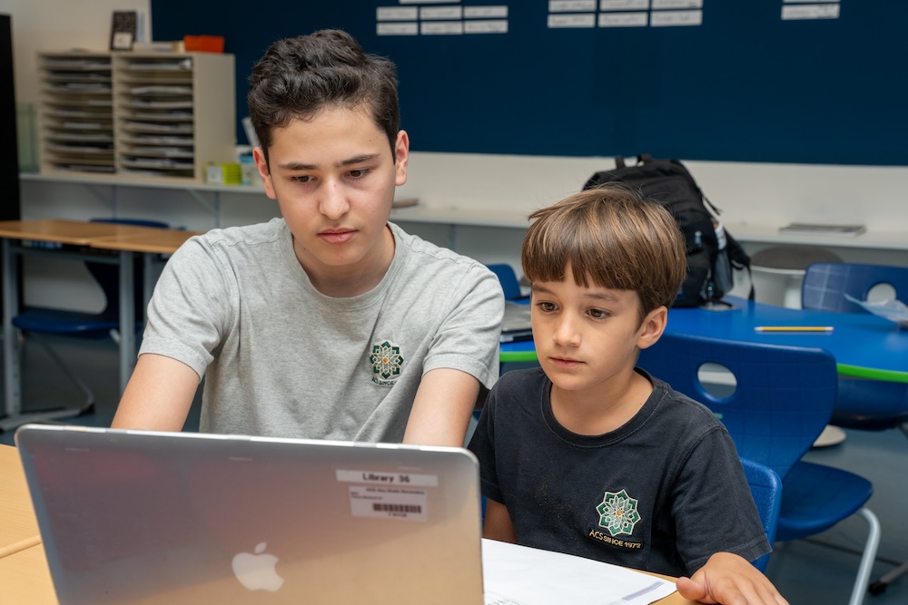High School student with Elementary School student working together at a laptop